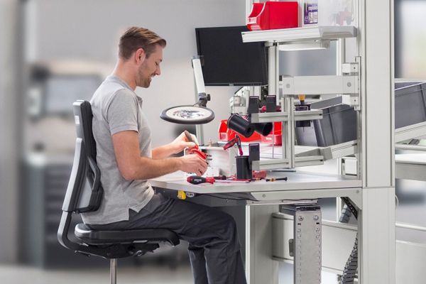 Ein junger Mann sitzt an einem ergonomisch ausgestatteten Industriearbeitsplatz.
